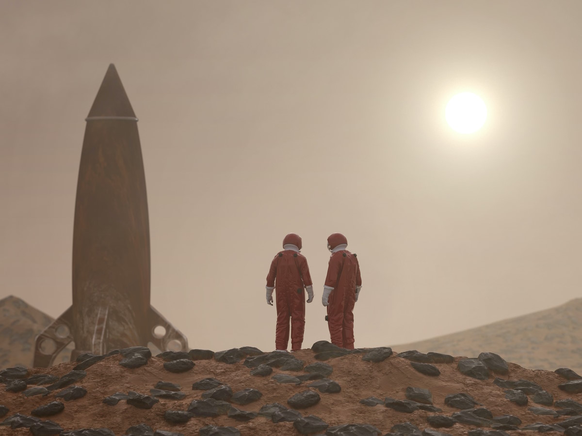 2 Personen stehen im Raumanzug vor einer Rakete.