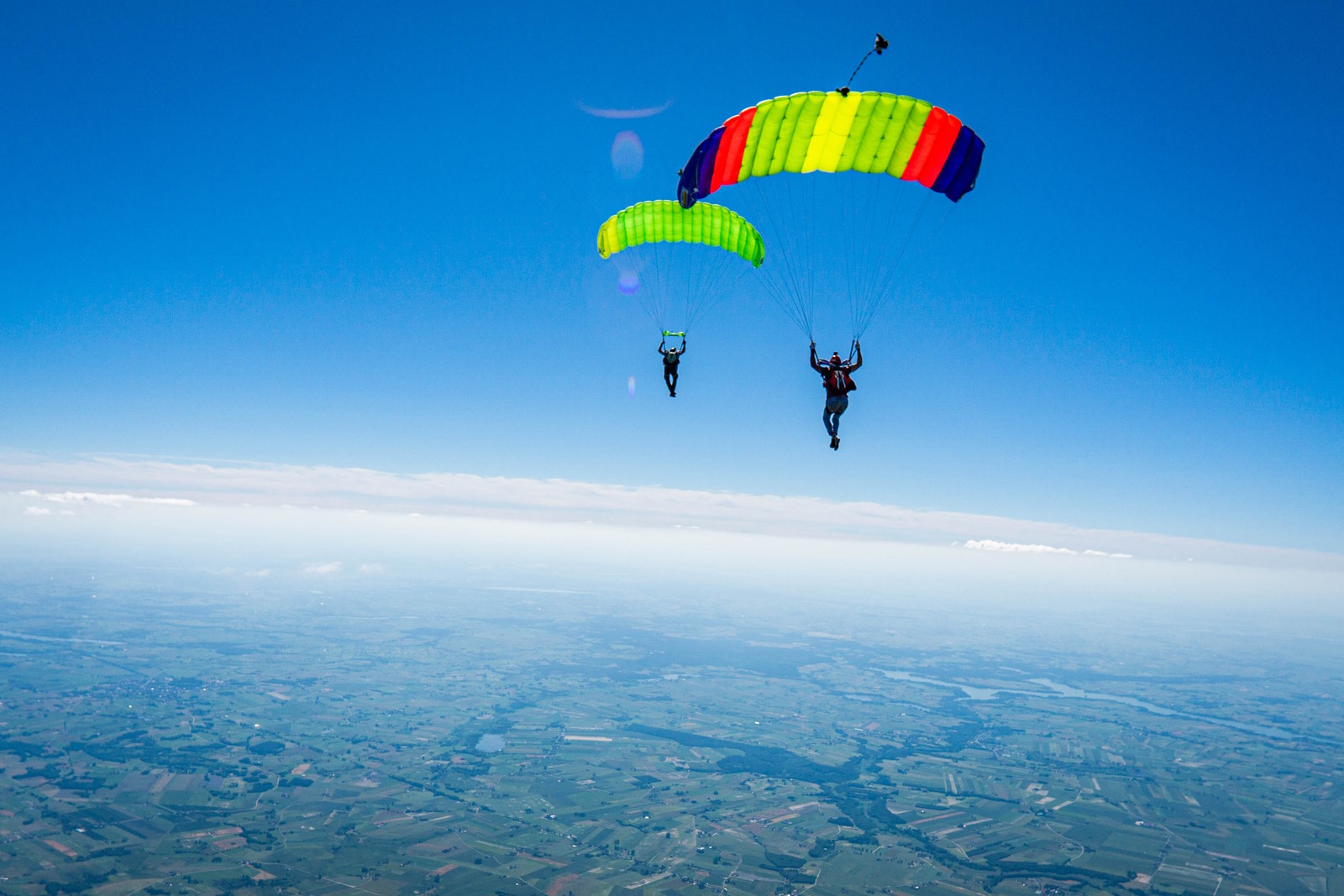 2 Personen schweben jeweils mit einem Fallschirm hoch über der Erde.